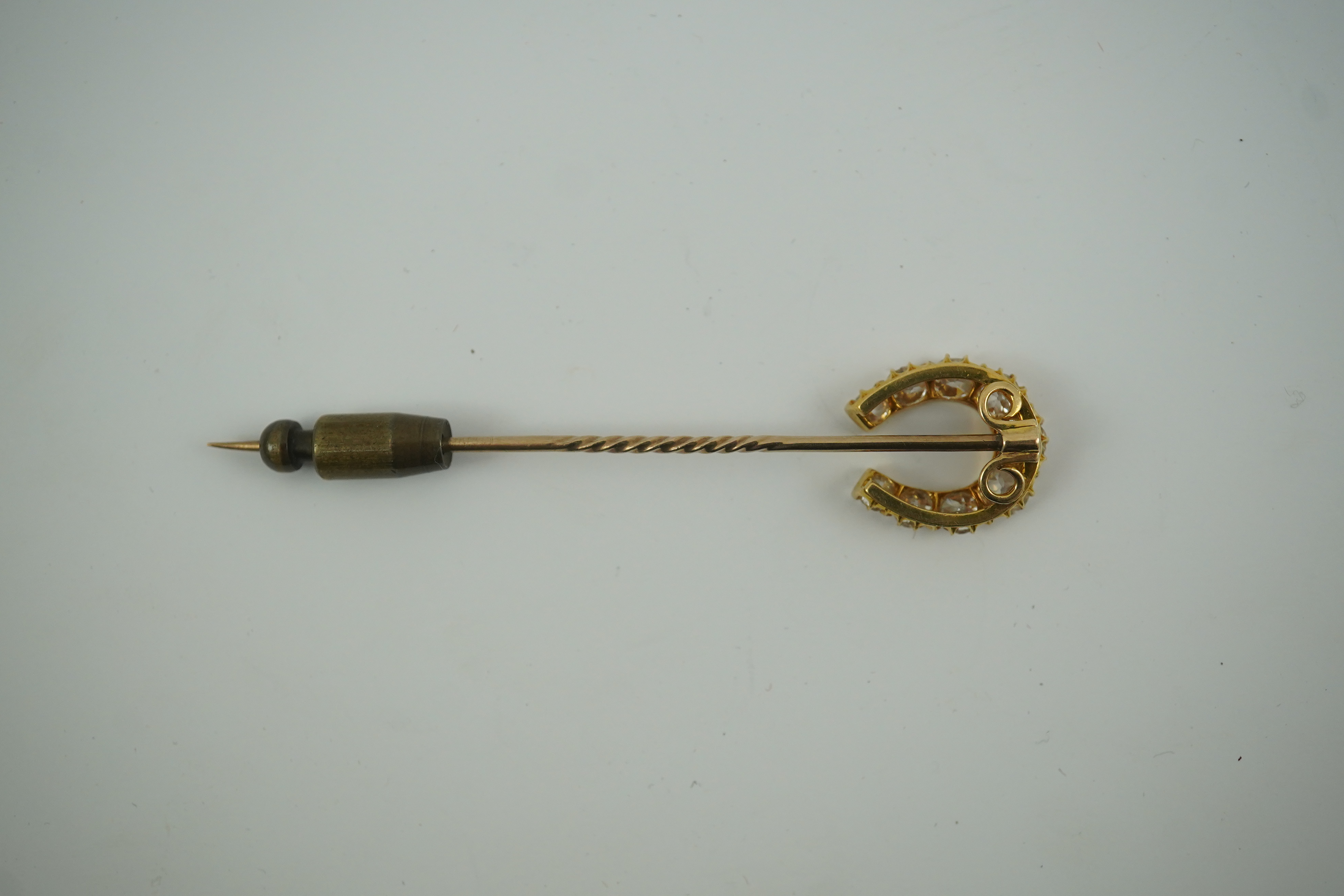 An early 20th century gold and nine stone graduated old cut diamond set horseshoe stick pin